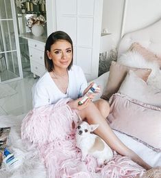 a woman is sitting on her bed holding a dog and looking at the camera while she reads