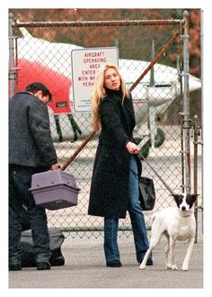 a woman standing next to a white and black dog on a sidewalk near a fence