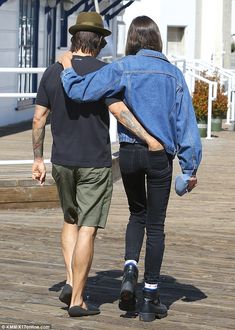 the man and woman are walking together down the boardwalk with their backs to each other