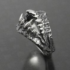 a silver ring with an animal's head on the front and side, sitting on top of a black surface