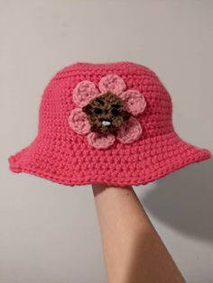 a crocheted pink hat with a flower on the side and a small brown teddy bear in the center