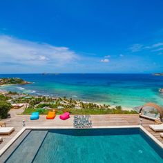 an outdoor swimming pool with lounge chairs and the ocean in the background