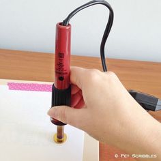 a hand holding a red lipstick in front of a piece of paper with writing on it