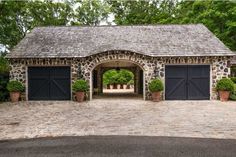 a stone building with two garages and potted plants on the driveway in front of it