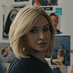 a woman with blonde hair standing in front of a wall full of posters and pictures