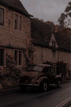 an old car is driving down the road in front of a house with ivy growing on it