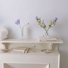 two vases with flowers are sitting on a shelf next to books and wine glasses