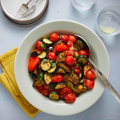 a white bowl filled with lots of different types of veggies next to silverware