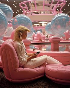 a woman sitting on top of a pink couch in a room filled with glass balls