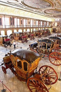 an old fashioned carriage is in the middle of a room filled with other antique carriages