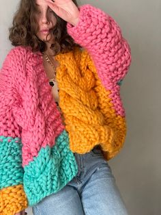 a woman wearing a multicolored sweater with her hands on her face and looking at the camera