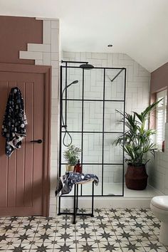 a bathroom with tiled floors and walls has a shower stall, potted plants, and a white toilet