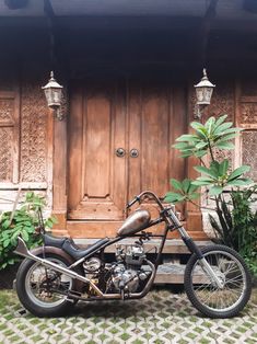 a motorcycle is parked in front of a wooden door and some plants on the sidewalk