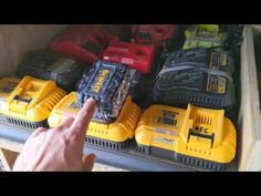 a man pointing at some yellow and black batteries in a storage bin with other tools