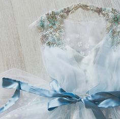 a white dress with blue ribbon and beading on the waist, sitting on a wooden surface