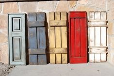 four different colored shutters are lined up against a stone wall