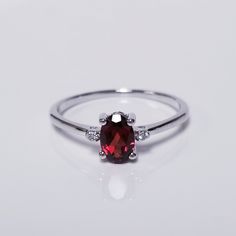 a close up view of a ring with a red stone and diamonds on the side