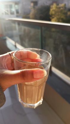 a hand holding a glass with water in it on top of a balcony overlooking the city