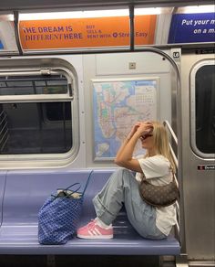 a woman sitting on a subway train with her hand in her hair, looking out the window