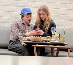 a man and woman sitting at a table looking at their cell phones while eating food