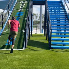 a man walking up the side of a green field next to a blue stair case