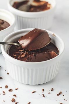 three white bowls filled with chocolate pudding and topped with a spoon full of melted chocolate