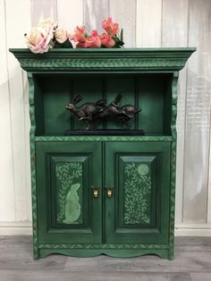 a green cabinet with flowers on top and two cats figurines in the front