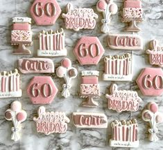 pink and white decorated birthday cookies on a marble counter top with candles, cake, flowers, and other decorations