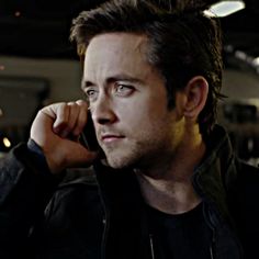 a man talking on a cell phone while wearing a black jacket and dark t - shirt