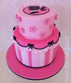 a three tiered cake with pink frosting and flowers on the top, sitting on a plate