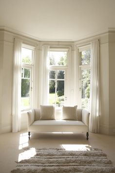 a white couch sitting in the middle of a living room next to two large windows