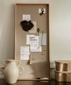 a cork board with papers and scissors on it in front of a white vase filled with flowers