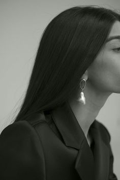 a woman with long dark hair wearing large silver hoop earrings and a black shirt is looking off into the distance