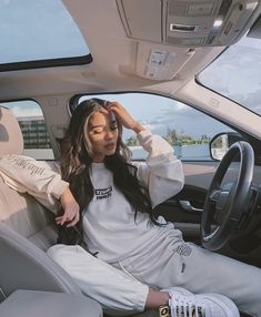 a woman sitting in the driver's seat of a car with her hand on the steering wheel