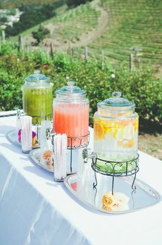 three jars filled with drinks sitting on top of a table next to a vineyard field