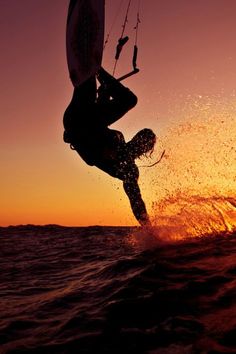 a person on a surfboard in the air above the ocean at sunset or sunrise