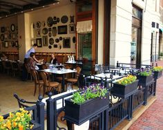 people sitting at tables in front of a restaurant with flower pots on the outside wall