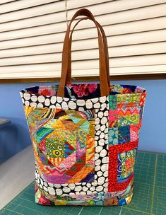 a multicolored tote bag sitting on top of a cutting board next to a window