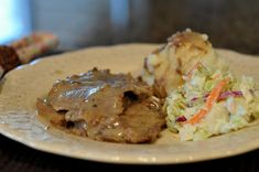 a white plate topped with meat covered in gravy next to coleslaw