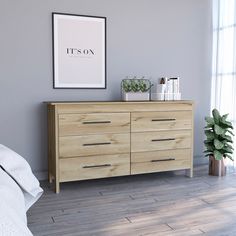 a bedroom scene with focus on the chest of drawers and a poster hanging above it