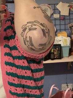 a woman with tattoos on her back holding a pink and green sweater over her shoulder