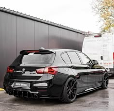 the back end of a black bmw car parked in front of a building with a van behind it