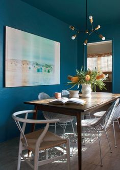 a dining room table with chairs and a book on it in front of a blue wall