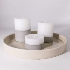 three white candles sitting on top of a tray with two grey and one white ones