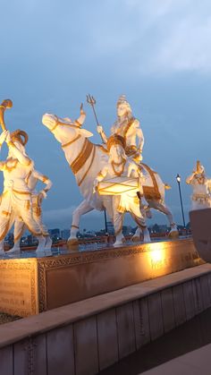 three statues of men riding horses in front of a building with lights on it's sides