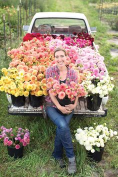 a woman sitting on the back of a truck filled with flowers