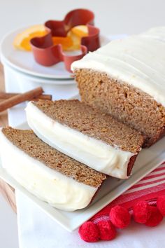 a loaf of cake on a plate with white frosting and oranges in the background