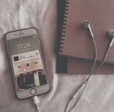 an iphone and headphones sitting on top of a bed next to a notebook with ear buds