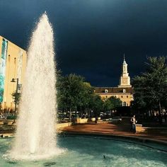 a large fountain in front of a building with a clock tower on it's side