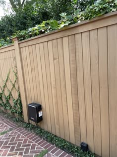 a mailbox on the side of a wooden fence next to a brick walkway and tree